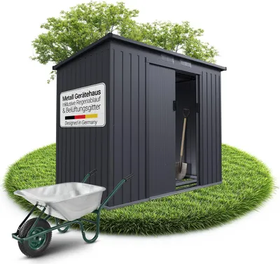 A dark gray metal garden shed is shown on a circular patch of grass, with a wheelbarrow in the foreground. Trees are visible in the background.