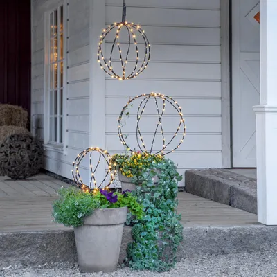 Three illuminated spherical decorations are displayed on a porch with potted plants.