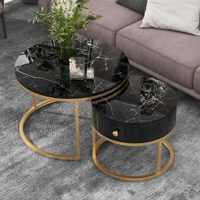 A set of two round coffee tables with black marble tops and gold metal legs are placed on a gray carpet next to a pink sofa.