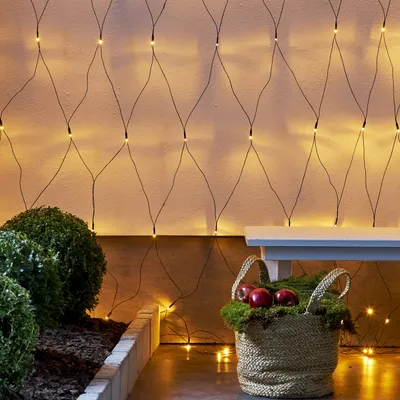A string of LED lights draped on a wall, with a basket of apples and greenery in the foreground.