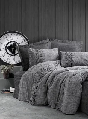 A bed with grey bedding and pillows, a large clock in the background.