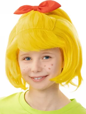 A child wearing a yellow wig with a red bow and a green shirt, smiling at the camera.