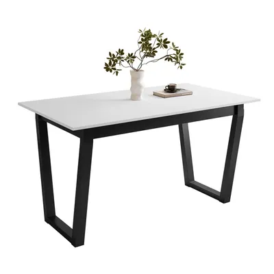 A white tabletop with black V-shaped legs, decorated with a vase of green leaves and a small book with a cup on top.