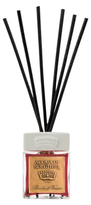 A reed diffuser with black reeds in a glass bottle with a gold and red label.