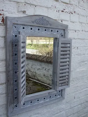 A decorative mirror with shutter-like sides mounted on a white brick wall.
