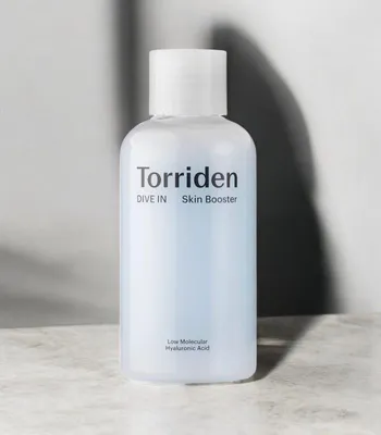 A product shot of a skincare bottle against a textured surface and a gray background with shadows.