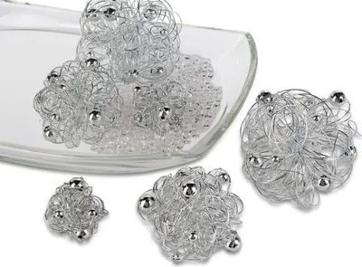 Several decorative wire balls with silver beads are arranged on a clear glass dish filled with small clear beads, with some balls outside the dish.