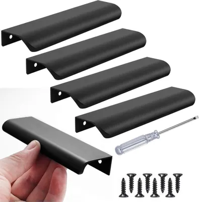 A hand is holding a black cabinet handle, with other similar handles arranged in the background, along with screws and a screwdriver.