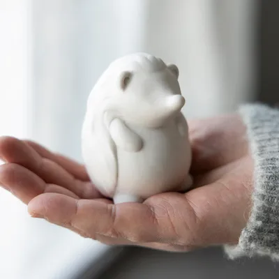 A small white ceramic hedgehog figurine is held in a person's open palm.