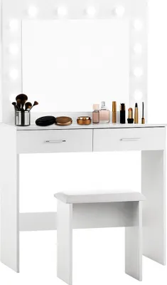 A white vanity table with a mirror and lights, two drawers, and a stool, with makeup products on top.