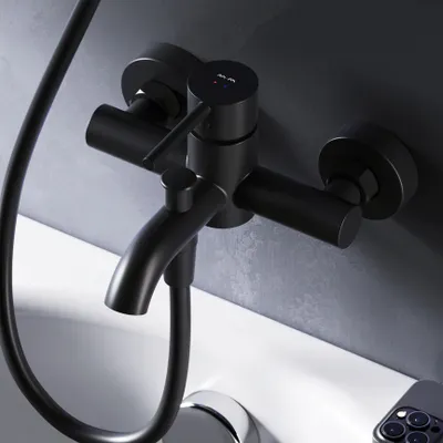 A close-up shot of a black bathtub faucet mounted on a gray wall, with a white bathtub visible below.
