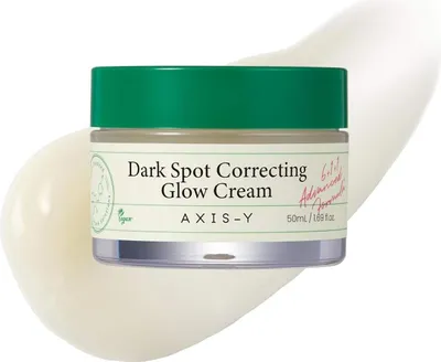 A jar of AXIS-Y Dark Spot Correcting Glow Cream is shown on a white and cream background, with a dollop of cream artfully placed behind it.