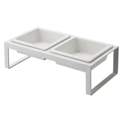 A white, elevated double pet bowl stand with two square ceramic bowls.