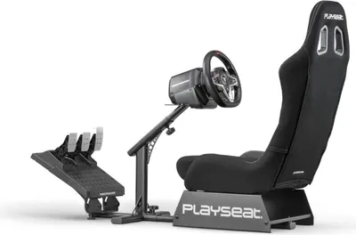 A black racing simulator seat with a steering wheel and pedals, shown from a three-quarter angle against a white background.