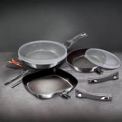 A set of cookware, including frying pans and detachable handles, arranged on a textured surface.