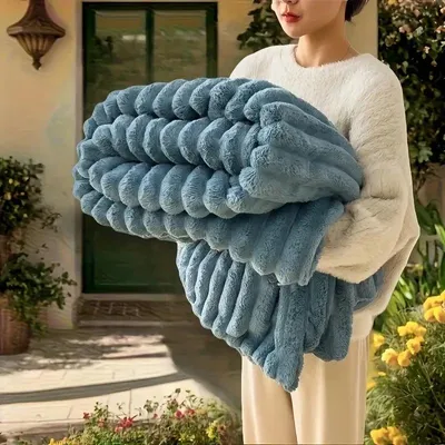A person holding a folded blue blanket in front of a house.