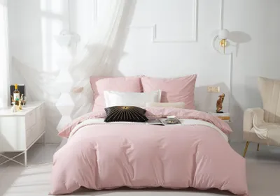 A neatly made bed with pink bedding and decorative pillows in a bright, minimalist room.