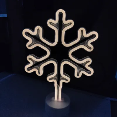 A neon snowflake decoration on a stand, lit with white light, against a dark background.