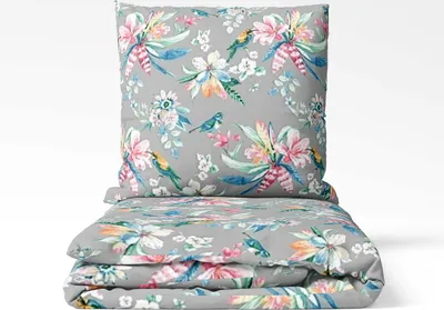 A folded bedding set and a pillow with a floral and bird pattern on a gray background.
