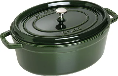A green oval Staub cast iron pot with a silver knob on its lid, shown from a slightly elevated side angle on a white background.