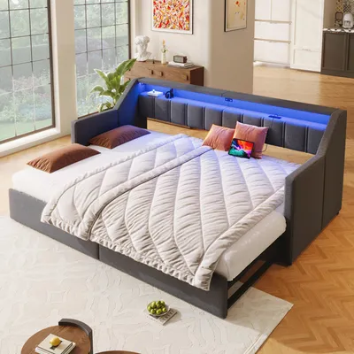 A daybed with an extended mattress, set up in a well-lit room with large windows and modern furniture.