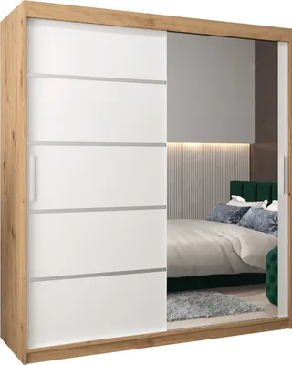 A bedroom scene reflected in a mirrored wardrobe door, showing a bed with green headboard and pillows.