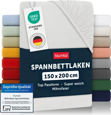 A stack of folded fitted sheets in various colors, with a white fitted sheet prominently displayed in the foreground with product information labels.