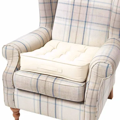 A close-up view of a cream-colored cushion placed on a plaid armchair.