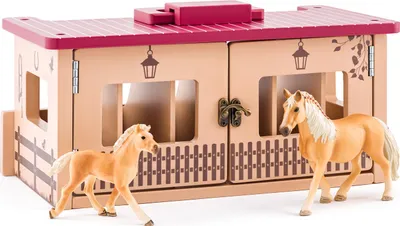 A toy horse stable with two toy horses in front of it.