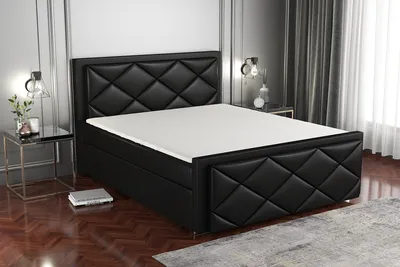 A black upholstered boxspring bed with a white mattress and topper is shown in a bedroom setting.