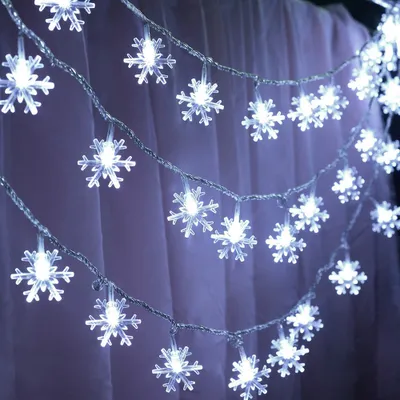 A string of snowflake-shaped lights against a purple curtain background.