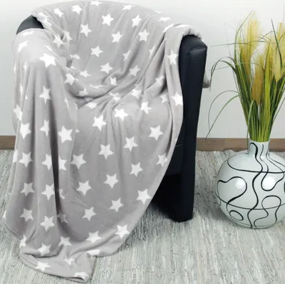A grey blanket with white stars draped over a black armchair, next to a decorative vase with tall grass.