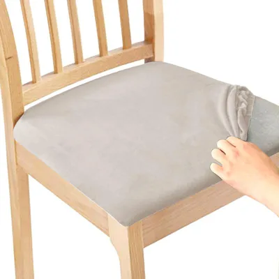 A hand is shown placing a beige seat cover onto a wooden chair.