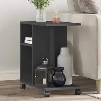 A dark gray side table with wheels is placed next to a light-colored sofa. The table has shelves and is decorated with vases and a lantern.