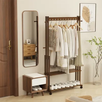 A well-lit room interior featuring a wooden garment rack with clothes and shoes, a full-length mirror, and a small storage bench.