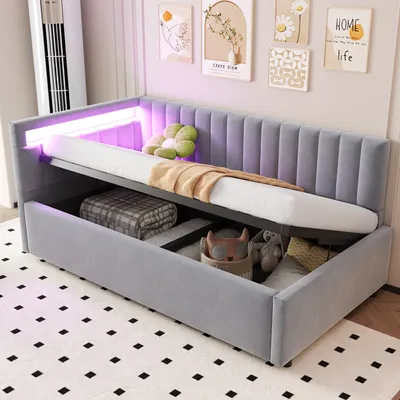 A grey upholstered daybed with its storage compartment open, revealing blankets and stuffed toys. The daybed has LED lighting along the headboard.