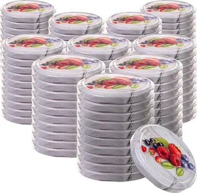 A stack of round metal lids with fruit designs, with one lid in the foreground.