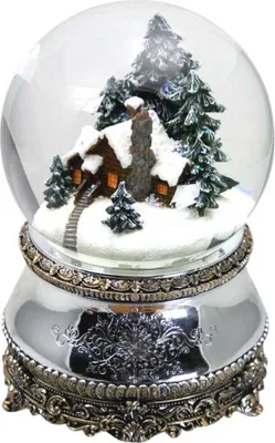 A snow globe with a miniature log cabin and pine trees covered in snow, set on a decorative silver base.