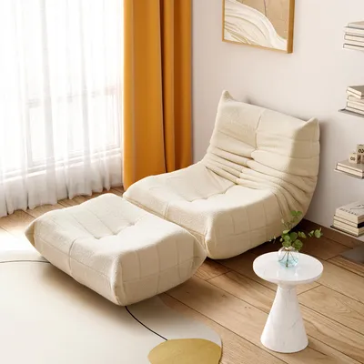 A beige armchair and ottoman are placed in a room with yellow curtains and a small white side table.