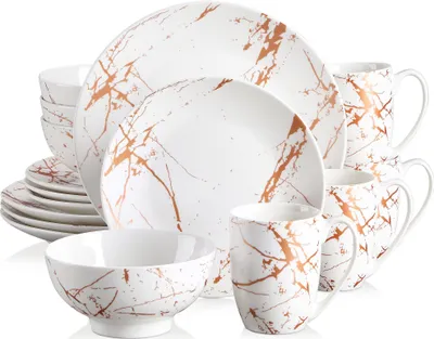 A collection of white ceramic dinnerware with a copper marble pattern, including plates, bowls, and mugs, arranged in a studio setting.