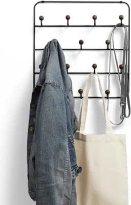 A black metal coat rack with wooden knobs mounted on a white wall, holding a denim jacket, a canvas tote bag, and a dog leash.