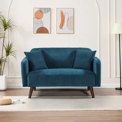 A blue corduroy sofa with two pillows is shown in a well-lit room with modern art on the wall.