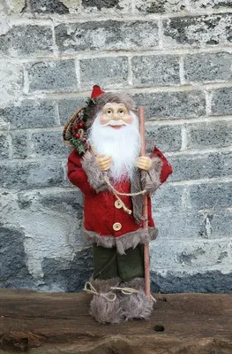 A standing Santa Claus figure with a sack on his back and a stick in his hand, against a brick wall.