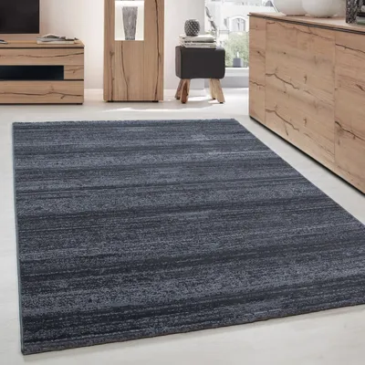 A dark gray rug with a subtle linear texture is laid out on a light-colored floor in a modern living room setting. Furniture pieces, including a wooden cabinet and a small stool, are visible in the background.
