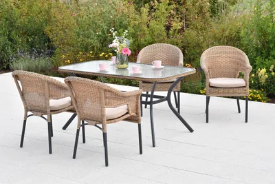 A patio dining set with four chairs and a glass-topped table, set on a light-colored patio with greenery in the background.