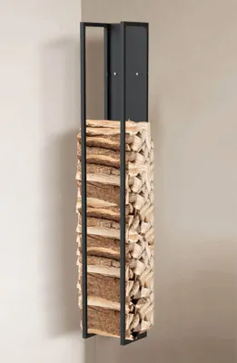 A tall, narrow metal firewood rack filled with logs, standing in a corner against a light-colored wall.