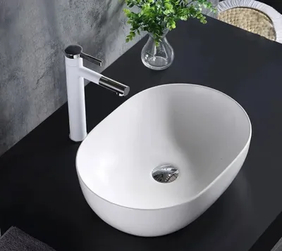 A white oval countertop sink with a white faucet on a black countertop.