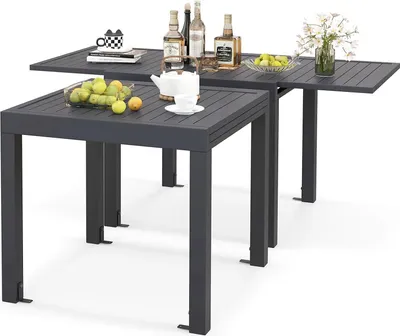 Two dark gray outdoor tables, one partially extended, are shown against a white background. The tables are set with decorative items like bottles, a teapot, and fruit.