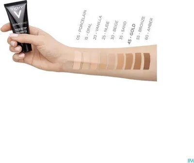 A hand is holding a tube of foundation, with swatches of different shades on the arm.