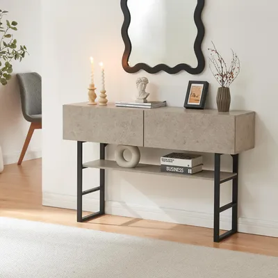 A console table with two drawers and a shelf, decorated with candles, a bust, a framed picture, and a vase with branches. A chair is visible in the background.
